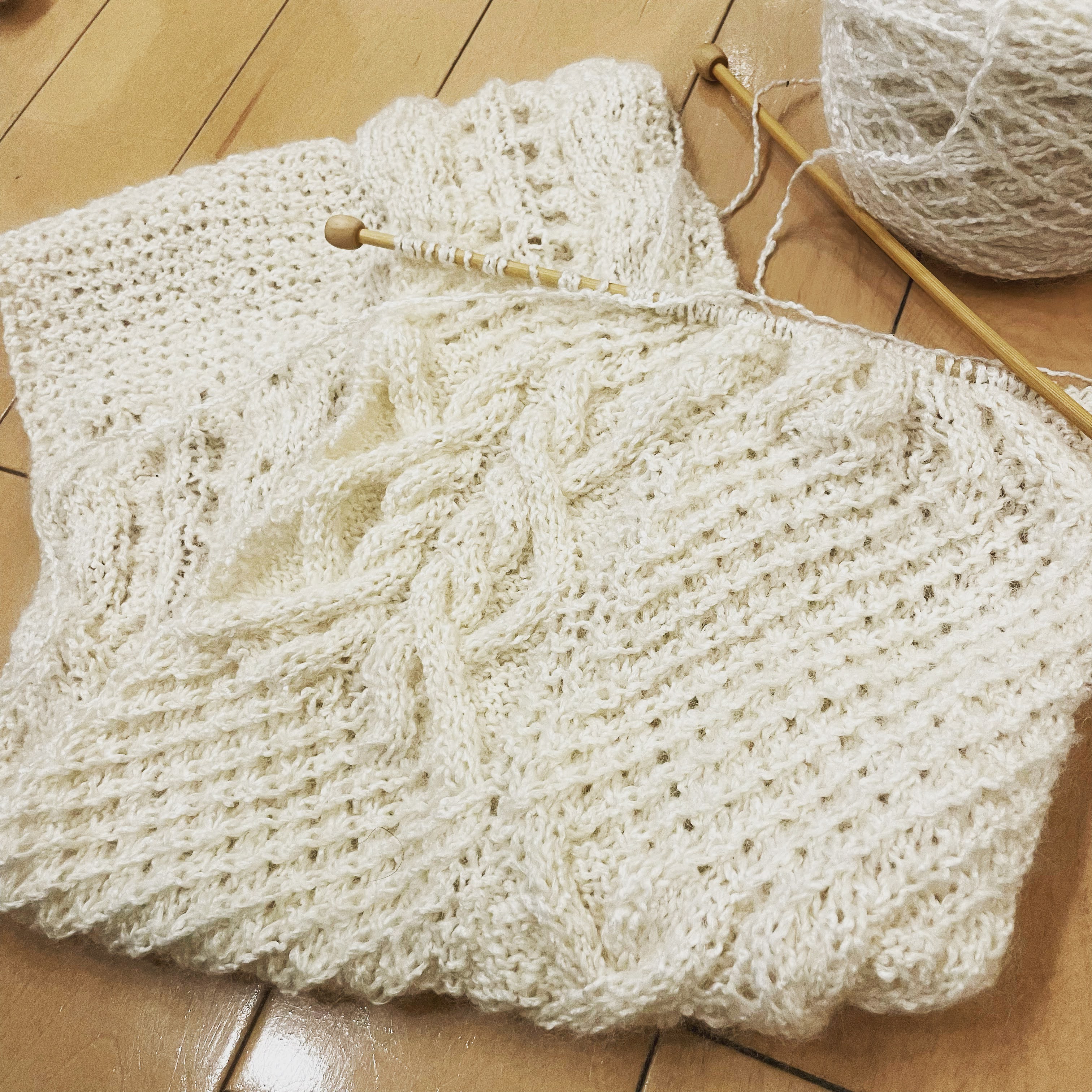 編み物をしている手元——ケーブル編みの編み地と竹針と毛糸