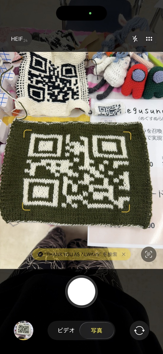 ブースに並べた編みQRコードをスマートフォンのカメラで読み取っているところ。画面に黄色い検出枠が出て、下に「THANK YOU AS ALWAYS を検索」と表示されている
