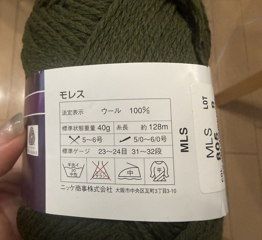 深緑の毛糸のラベル。ウール100%、標準状態重量40g、糸長約128m、棒針5〜6号、かぎ針5/0〜6/0号、標準ゲージ23〜24目31〜32段と印刷されている