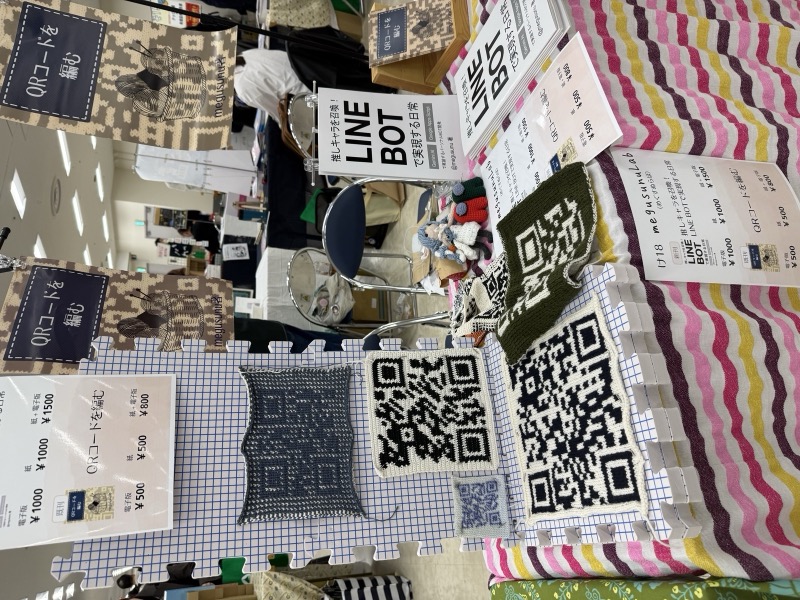 け18ブースの様子——QRコード編み作品とLINE BOT本が並ぶ